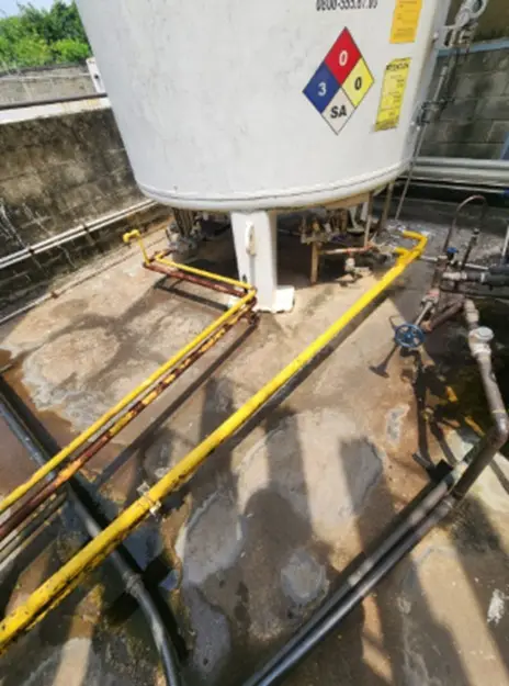 Tuberías corroídas y desordenadas junto a un tanque de proceso